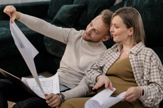 A couple sitting on a sofa reviewing architectural blueprints, symbolizing home buying or renovation.