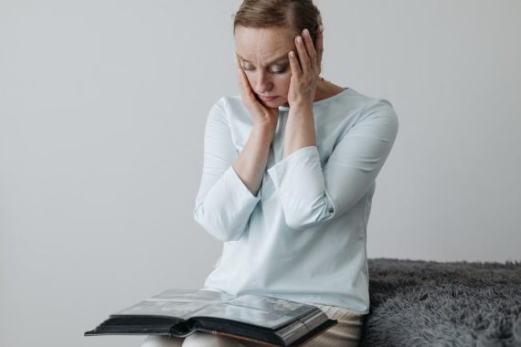 A woman sits thoughtfully with her hands on her face, looking at a photo album.